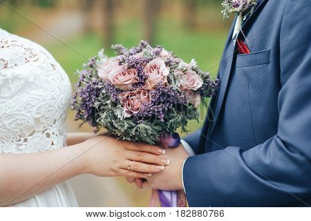 The bride and groom put their own hands with rings on beautiful wedding bouquet
