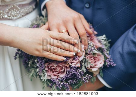 The bride and groom put their own hands with rings on beautiful wedding bouquet