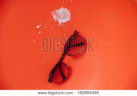 Sunglasses and white abstract blot of kefir butter milk yogurt or turkish drink ayran with splashes and drops on orange background. Blemish and grunge. Vision and protection