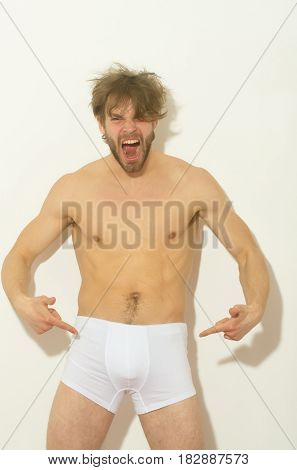 Angry man or sexy muscular macho athlete with fit naked torso shouting and finger pointing at white briefs on wall background. Male underwear fashion and fitness