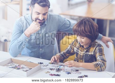 Having a tremendous time. Smiling dad and son building puzzle together while enjoying family time at home