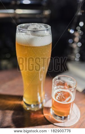 Light beer in a beer glass and dark beer in a small glass on a wooden bar counter.Vertical frame.view from above