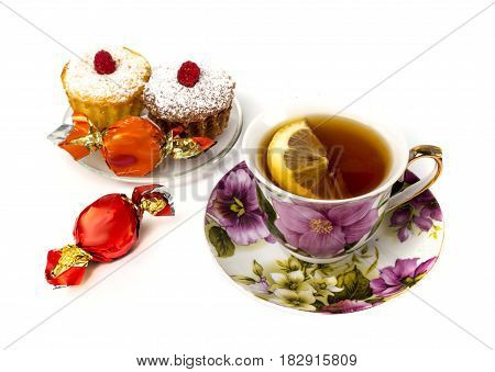 Mug of tea with lemon and and two cupcakes on isolated white background