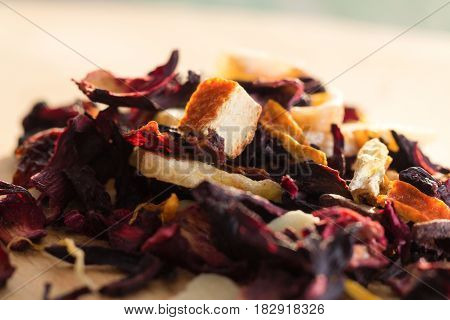 Pile of fruit tea with petals and dry fruit .The composition of the heap of tea leaves and dried hibiscus flower located on a wooden Board. Tea with natural ingredients closeup. Macro photo of tea.