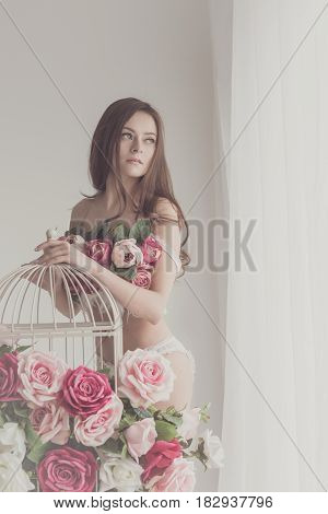 Lovely girl in lingerie. Bra of flowers. Spring mood. She stands by the empty cage near the window. Soft focus.