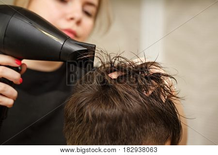 Professional hairdresser doing haircut men's hair. Drying hair with a hairdryer. Beauty saloon. Male beauty. The client is a hipster.