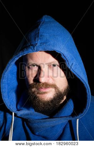 Solid bearded middle-aged man in a hood  portrait on black background