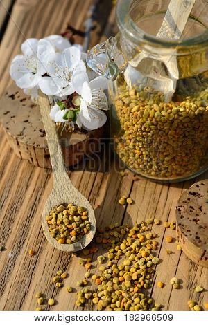 Grains of bee pollen in jar and wooden spoon on wooden table. Bee products. Apitherapy