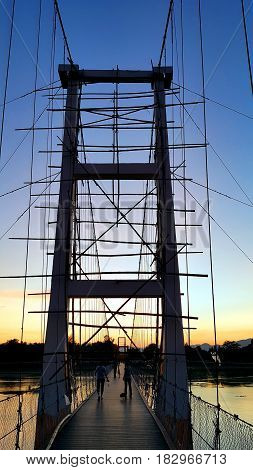 Underconstruction hanging bridge (200 year Rattanakosin Sompoch bridge) across the ping River during colorful twilight sky. Tak province Thailand