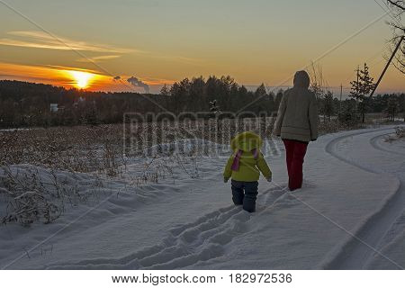 Mother and her little daughter walking through a snowy field. Мать и дочь идут на фоне заката.