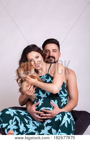 Happu pregnant woman with her husband and dog in studio photo. Wife and husband. Parenthood and expecting baby