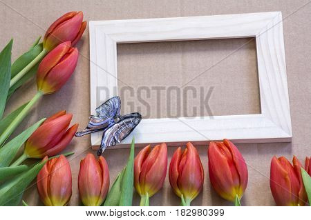 Blue glass butterfly on the wooden frame with many red tulips around