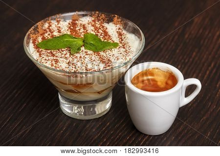 Tiramisu creme cake dessert in glass with mint leaves and coffee cup on black wooden background