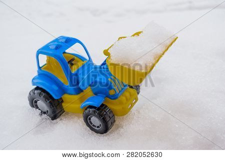 Toy Tractor With Front Loader In The Snow. Concept Of Utilities And Snow Removal. Road Services.