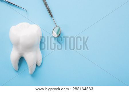 Professional Steel Dental Instrument With A Mirror Near White Tooth Model On Light Blue Background W