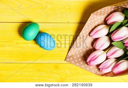 Easter Is Coming. Colorful Bright Eggs And Bouquet Fresh Tulip Flowers On Yellow Background Top View