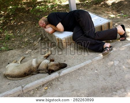 Odessa, Ukraine - Summer 2018: A Drunk Unshaven Man In Black Clothes Fell Asleep On The Ground Next 