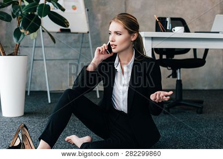 Barefoot Businesswoman Sitting On Floor And Talking On Smartphone With Emotion