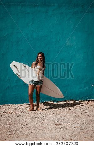 Happy Surfer Girl With Surfboard In Front Of Blue Wall