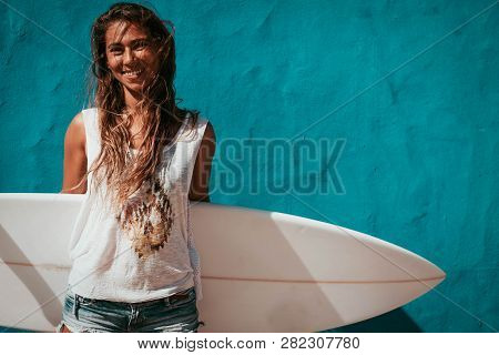 Happy Surfer Girl With Surfboard In Front Of Blue Wall