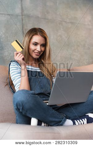 Beautiful Woman Holding Credit Card And Sitting On Sofa With Laptop