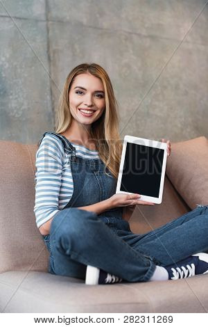 Young Girl Sitting On Sofa And Showing Blank Screen Of Digital Tablet