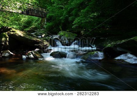 Long Exposure Of A Waterfall Flowing Under A Bridge  At Watersmeet In Devon