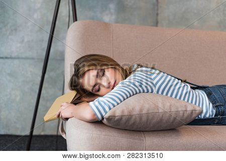 Young Beautiful Woman Sleeping On Pink Sofa With Book In Hand