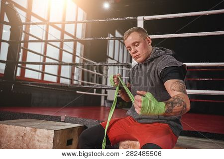 Never Give Up. Strong Tattooed Athlete In Sports Clothing Wrapping Hands With Green Boxing Wraps In 