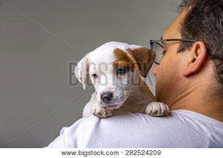 Horizontal Portrait Of Handsome Cheerful Man Holds Jack Russell Terrirer On His Shoulder, Has Glad E