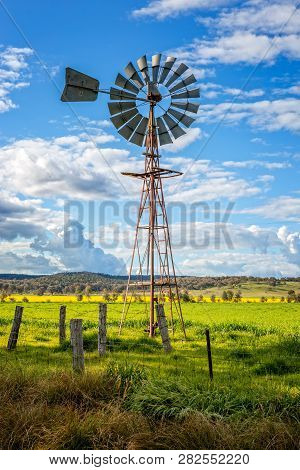Southern Cross Windmill In A Rural Field With Crops Growing Under A Blue Sky