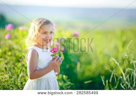 A Little Girl Wearing Flower Yellow Dress With White Hat And Stand In The Yellow Flower Field Of Sun