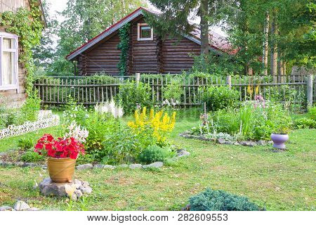 Country House Made Of Dark Logs And Beautiful Garden With Blooming Flowers In Summer. Karelia, Russi