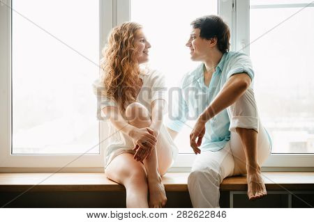Happy Girl And Man Hugging Near Window In Home. White And Blue Clothes. Valentine Day.