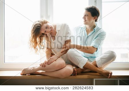 Happy Girl And Man Hugging Near Window In Home. White And Blue Clothes. Valentine Day.