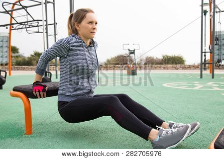 Tensed Fit Girl Exercising Her Arms Outdoors. Young Woman In Hoody And Tights Doing Triceps Dips On 
