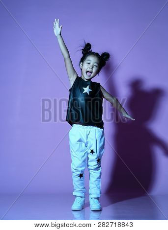 Joyfull Asian Kid Girl In Shirt And Pants With Stars And White Sneaker Stands With Her Hand Up And S