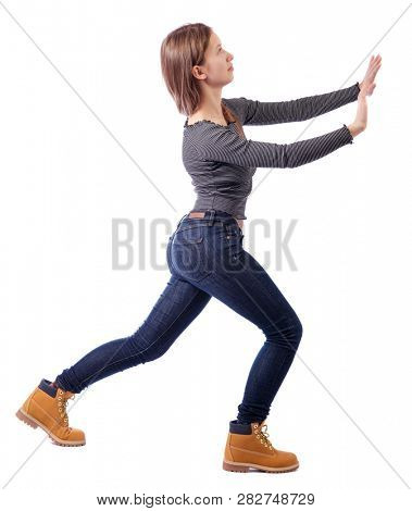 back view of woman pushes wall.  Isolated over white background. Rear view people collection. backside view of person. A girl in jeans and boots is pushing something in front of her.