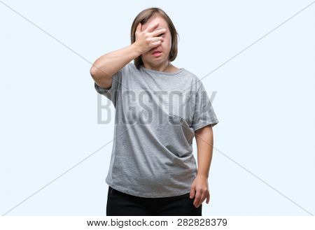 Young adult woman with down syndrome over isolated background peeking in shock covering face and eyes with hand, looking through fingers with embarrassed expression.