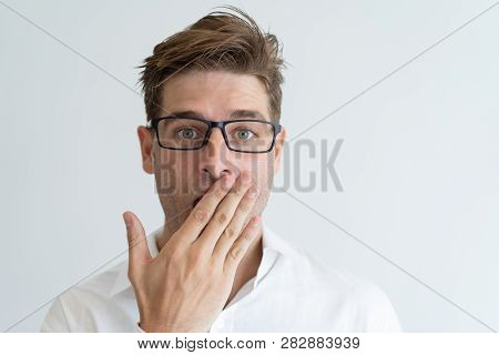 Surprised Handsome Man Covering Mouth With Hand. Embarrassed Young Guy Wearing Glasses And Looking A