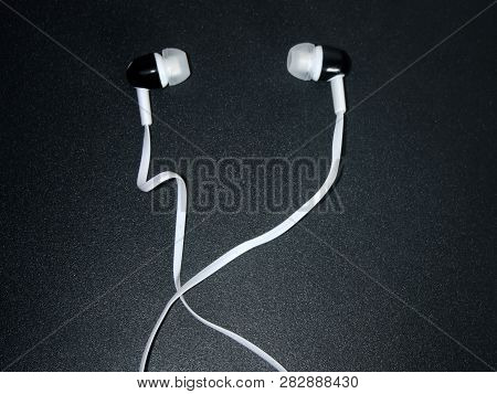 White Headphones With Black Inserts With A Long White Wire On A Black Surface