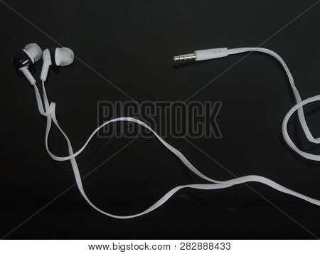 White Headphones With Black Inserts With A Long White Wire On A Black Surface
