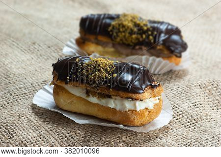 Eclairs With Pistachio And Black Chocolate And White Chocolate With Custard On Wooden Background And
