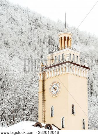 The Clock Tower On The Background Of The Mountain With Snow-covered Trees