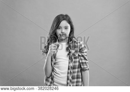 Serious Kid With Funny Party Moustache. School Girl Ready For Fun. Happy Childhood. Child Try To Mak