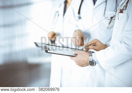 Group Of Unknown Doctors, Men And A Woman, With Stethoscopes, Discuss Medical Exam Resoults, Using A