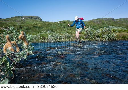 Hiking in Swedish Lapland. Man crossing river, Trekking alone in Sweden in summer. Arctic nature of Scandinavia in warm sunny day