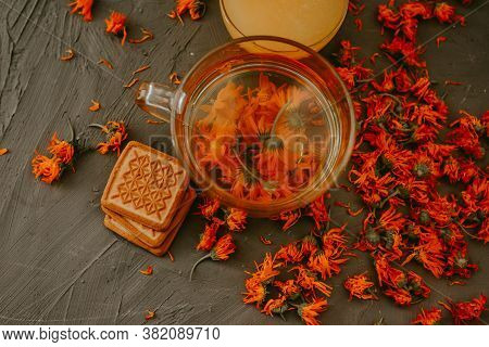 Tea With Calendula Flowers And Biscuits. Transparent Glass Cup And Saucer