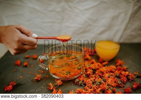 A Womans Hand Pours Honey From A Spoon Into A Cup Flower Tea