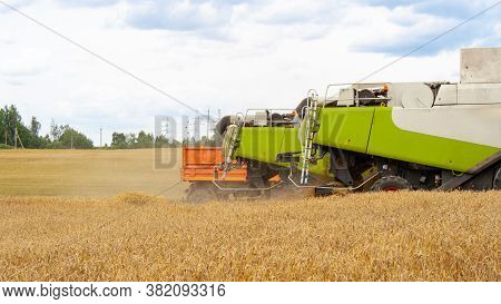 Backs Of Combines And Truck Trailer Lined Up In A Row In A Wheat Field Against A Blue Sky With Cloud